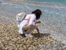 A woman in a bright dress dips her hand into the sea. Koper (`Ca