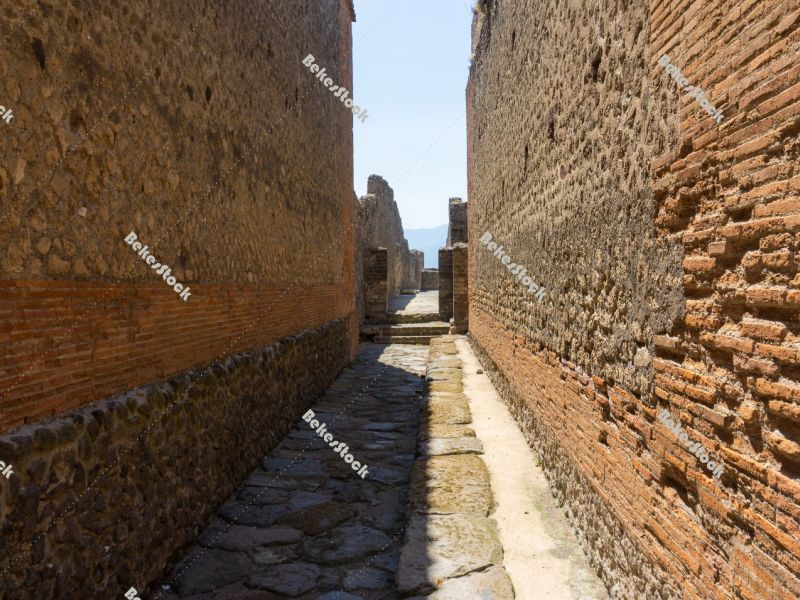 Alley way (`vicolo`) in Pompeii. The narrow street is lined with Alley way (`vicolo`) in Pompeii. The narrow street is lined with